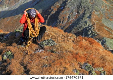 Climber sitting on mountain summit prepares the rope for transport