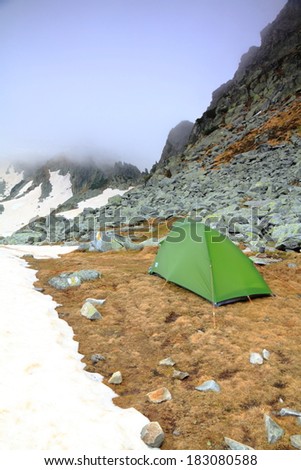 Cloud covered mountains and a green tent near the snow