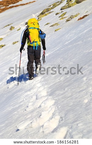 Sunny winter day with climber carrying heavy loads on the mountain