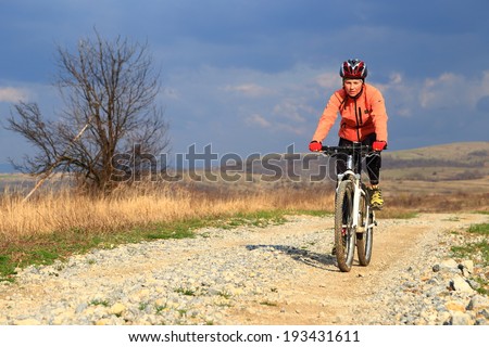 Woman rides a bike on dirt road in sunny spring day