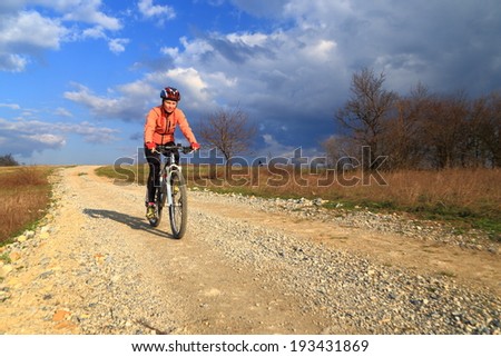 Woman rides a bike on dirt road in sunny spring day