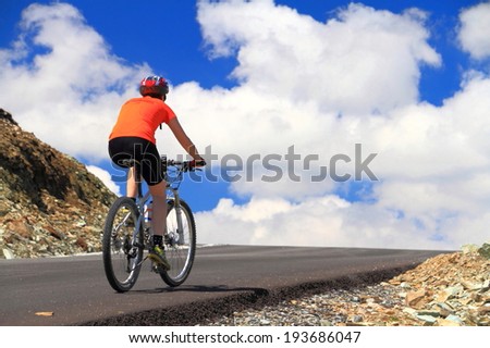 Woman cyclist ascending a mountain road to the sky and clouds