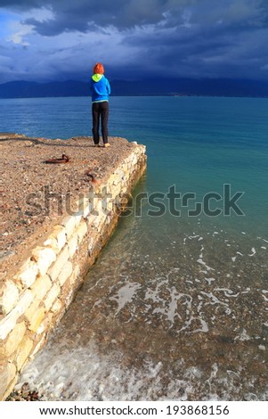 Cloudy sky with woman standing on a pier and watching the sea, Greece
