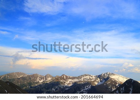 Sunny mountain landscape with summits spotted with snow under blue sky