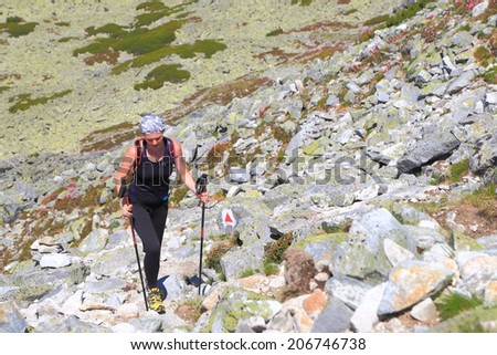 Hiker woman ascending sunny trail surrounded by grey boulders