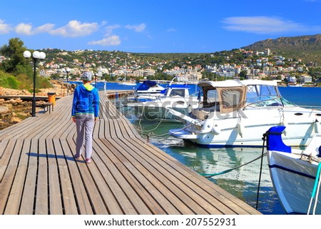 Tourist woman walking on wood deck of a small Greek harbor, Porto Rafti, Greece
