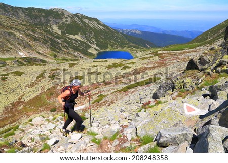 Hiker woman ascends on sunny mountain trail