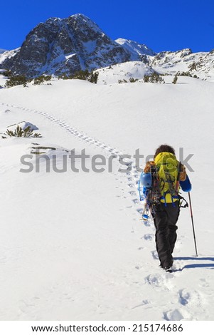Mountaineer carries climbing gear while following foot steps on a white snow field