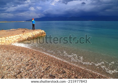 Single woman on a pier watching the sea under stormy clouds, Greece