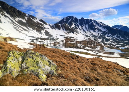 Sunlit boulders and snow patches on the mountains under white clouds