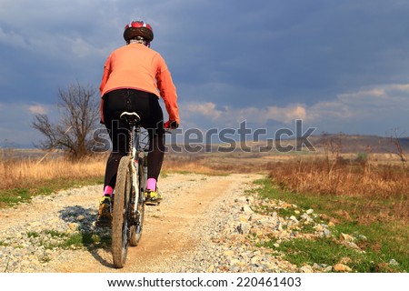 Woman riding a bike on rough road under gloomy sky