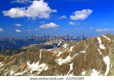 Spring day on the mountains with snow stripes on distant summits under white clouds
