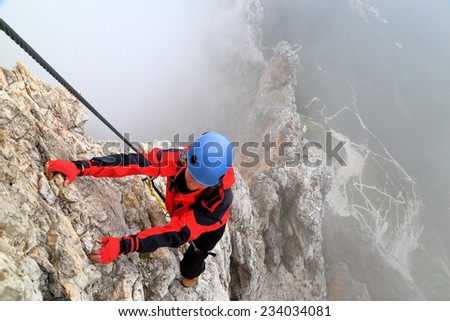 Cloudy weather and young woman climbs steep ridge on via ferrata \
