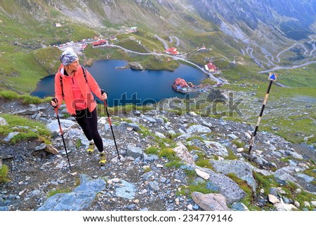 Hiker woman on rocky mountain trail high above glacier lake surrounded by chalets