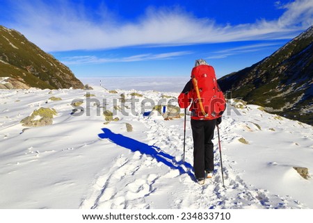 Snowy mountain with backpacker on a trail above clouds