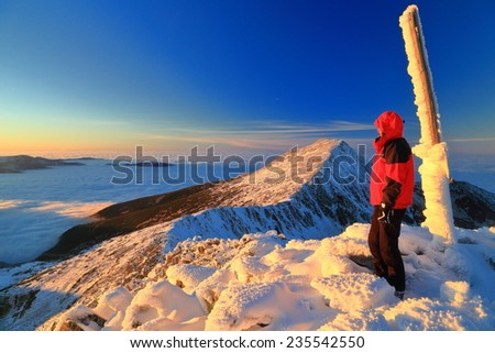 Sunset on the mountain summit and woman admiring the view during winter