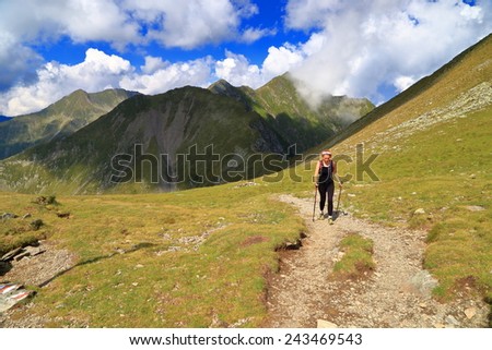 Hiker woman approaching on a mountain trail in sunny summer day