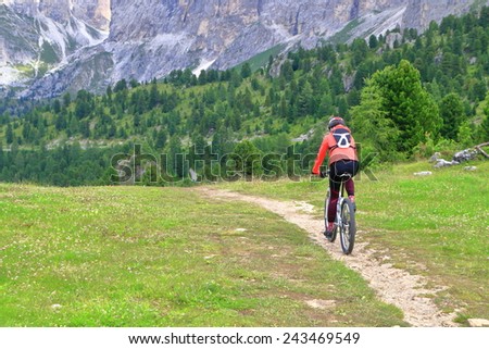 Woman cycling on narrow trail near Sella pass in overcast day, Dolomites Alps, Italy