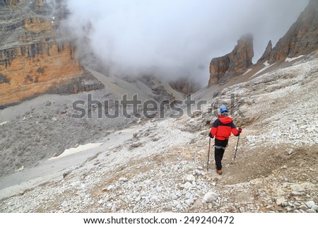 Woman climber descending towards cloud covered valley and Pomedes refuge, Tofana massif, Dolomite Alps, Italy
