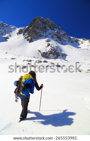 Mountaineer carries heavy backpack while ascending a sunny mountain slope in winter