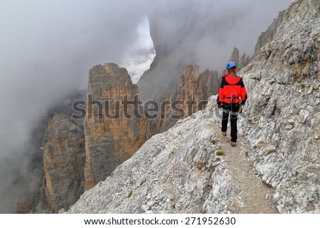 Dark clouds cover mountain slope with climber approaching on narrow path, Tofana massif, Dolomite Alps, Italy