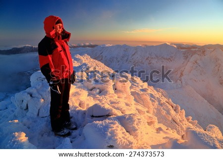 Woman mountaineer admires the sunset from a snow covered mountain summit above the clouds