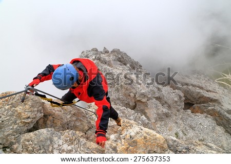Aerial rock wall with climber placing protection gear on the cable along via ferrata \