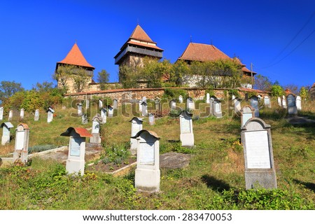 Sunny cemetery and distant church with medieval architecture on UNESCO world heritage list, Viscri, Transylvania, Romania