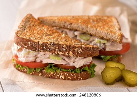 A delicious flaked white tuna salad sandwich with tomato, lettuce, mayonnaise, and pickles.