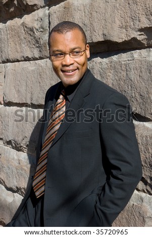 smiling businessman relaxes against the wall of a building