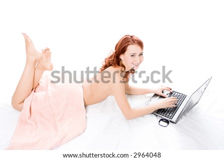 spa naked red beautiful girl lays on white covered by a pink towel and works on laptop