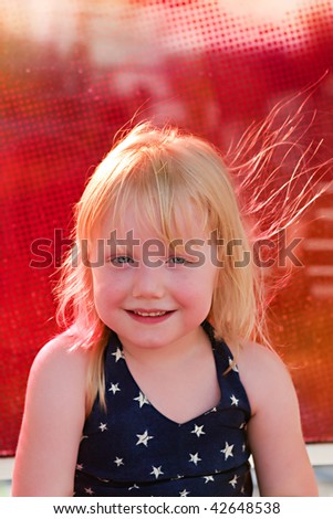 A young smiling girl with a star shirt and hair blowing in the wind