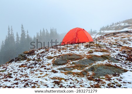Foggy morning with a red tourist tent on a hill with big grey stone