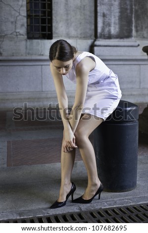 Terribly tired, a woman is sitting on a street, hanging her head and hands laying  on her knees/Fragile
