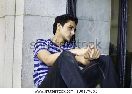 A young asian guy is sitting by a window glass and thinking/Portrait of a young asian guy