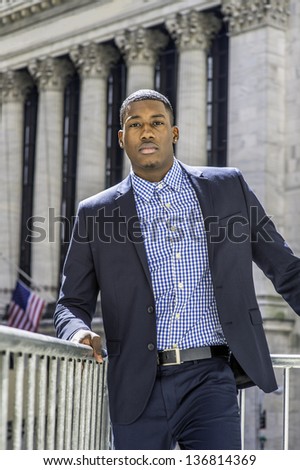 A young black businessman is standing in the front of a office building and confidently looking forward/Portrait of Young Black Businessman