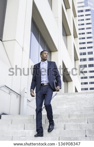 A young handsome black businessman is walking down on steps from a business building.