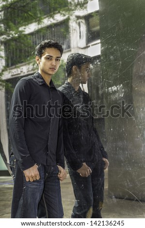 Dressing in a black shirt and a fashionable pants, a young asian teenager is standing by a mirror  wall, thoughtfully looking at you./Portrait of Young Asian Teenager