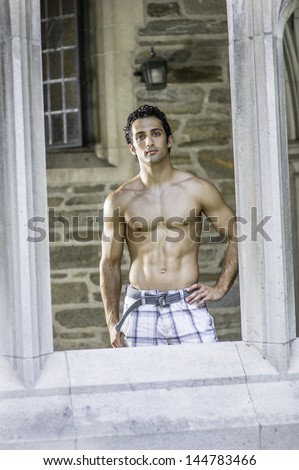 A young, handsome, muscular guy is  looking through an old fashion window fame./Portrait of Young Handsome Fitness Guy