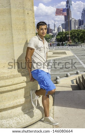 Dressing in a iron short sleeve shirt, blue shorts, a young attractive guy is standing by a column and looking at you. /Traveler