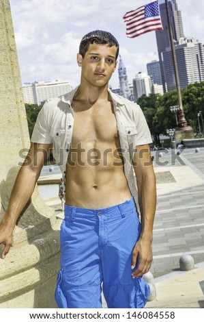 Dressing in short sleeve shirt unbuttoned, blue shorts, a young attractive guy is charmingly looking at you./Portrait of Young Guy