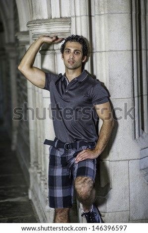 Dressing in a gray polo shirt, pattern shorts, a young strong handsome guy is standing by a old fashion wall, confidently looking forward. / Portrait of Young Fitness Guy