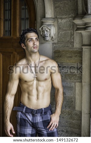 Wearing a cross necklace and half naked, a handsome, muscular guy is standing at a old fashion doorway and looking forward. / Portrait of  Fitness Guy