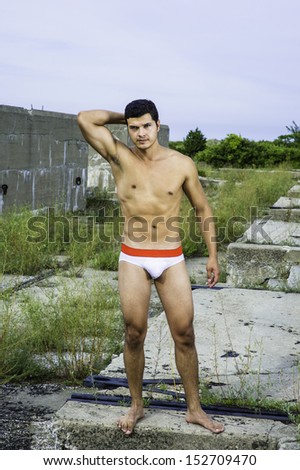 A masculine guy, wearing a red and white underwear, barefoot and half naked, is standing in a desolation land, confidently looking forward. /In the Land