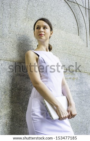 Dressing in a white sleeveless work clothes, holding a small computer,  a businesswoman is standing outside, looking forward. / Portrait of Businesswoman