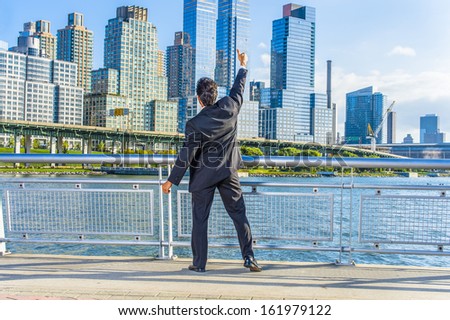 Facing dramatic high buildings of New York City, a middle age businessman is raising his arm and thumb up, a symbol of success. / Thumb Up