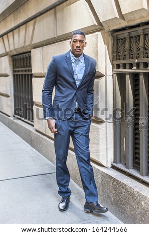 A young black businessman is standing outside by a window on a street and taking a break / Portrait of Young Black Businessman