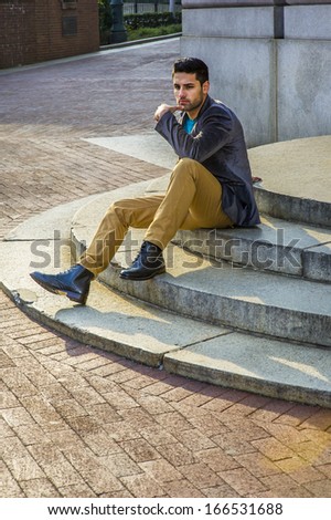 One hand touching his chin, a young handsome professor with bread and mustache is sitting on circle steps, relaxing and thinking / Relaxing and Thinking