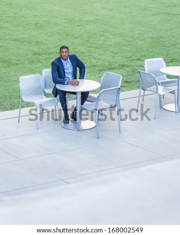 A young handsome black businessman is sitting on a chair by a green lawn and waiting for you. / Waiting for You