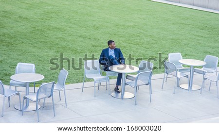 A young handsome black businessman is sitting on a chair by a green lawn and waiting for you. / Waiting for You